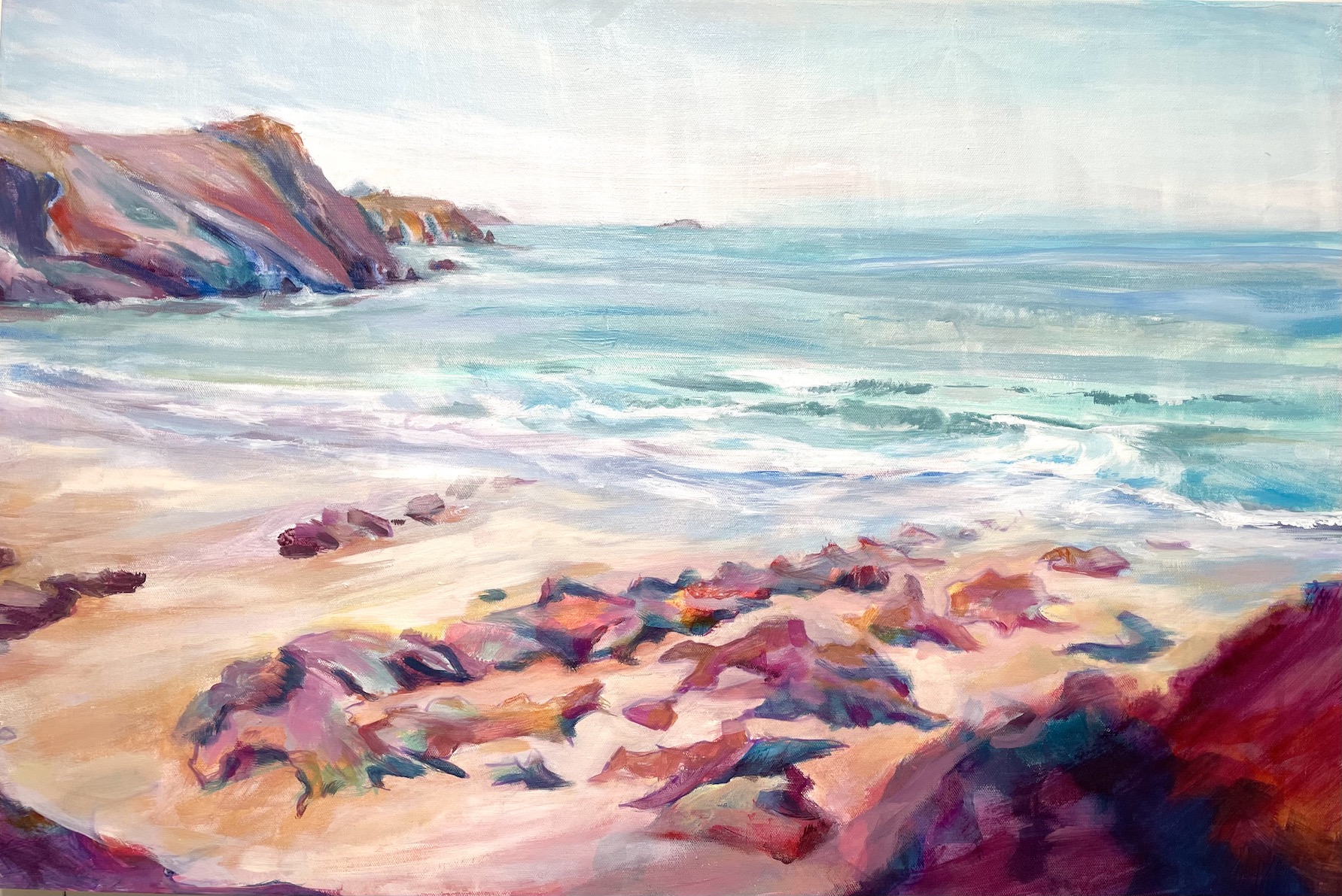 Kate Kelly Coastal Artist. A large original acrylic painting showing Treath Llfyn beach in Pembrokeshire. The deeply coloured rocks in magenta, rich blus and pinks form a c shape embracing the peach coloured sand. The sea with white edged incoming waves dominates the view full of light greeny blues and turquoises. The atmospheric sky is lightly coloured in teh the top quarter of the canvas and is a perfect foil to the sea, headland below.